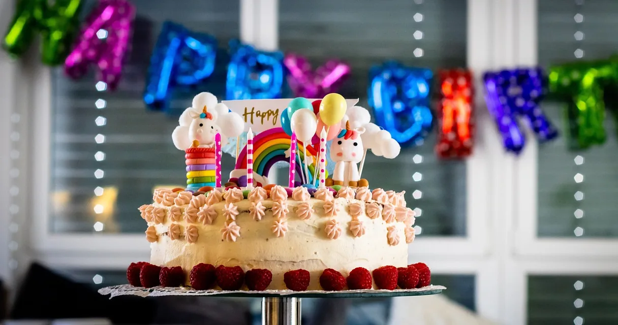 Bolo de aniversário infantil com velas e balões coloridos ao fundo