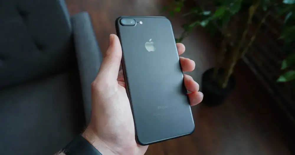 Mão segurando smartphone preto com a tela voltada para baixo