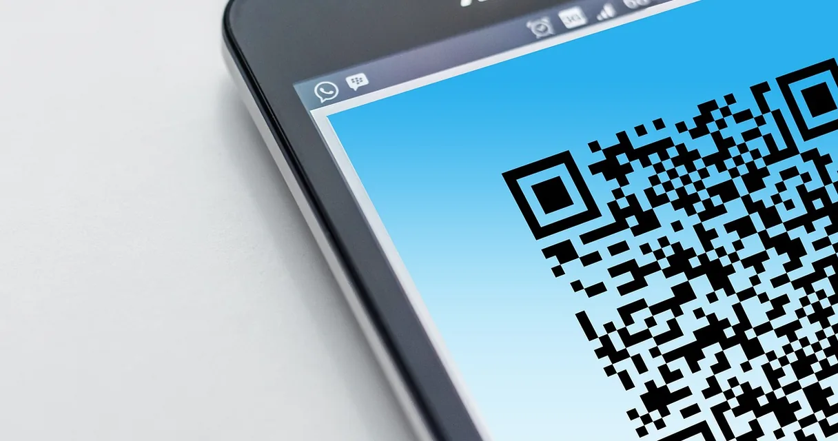 QR Code exibido na tela de um celular visto de perto sobre uma mesa clara